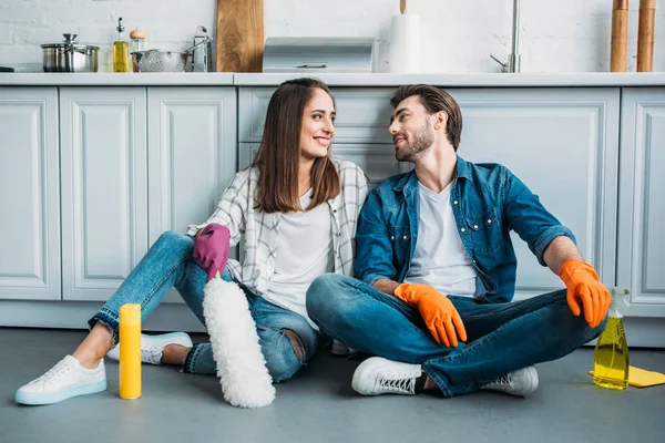 Glückliches Paar, das auf dem Boden sitzt und einander nach dem Putzen in der Küche ansieht — Stockfoto