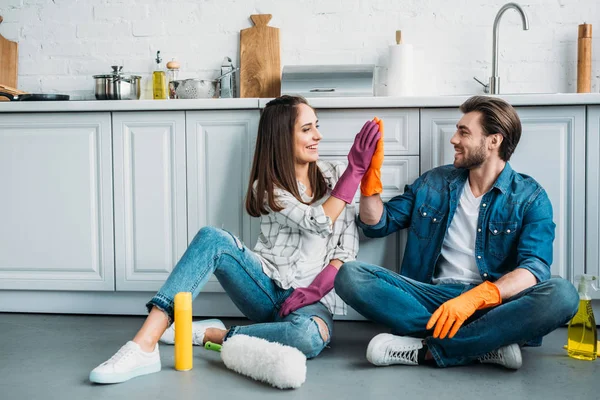 Пара сидит на полу и дает пять после уборки на кухне — стоковое фото