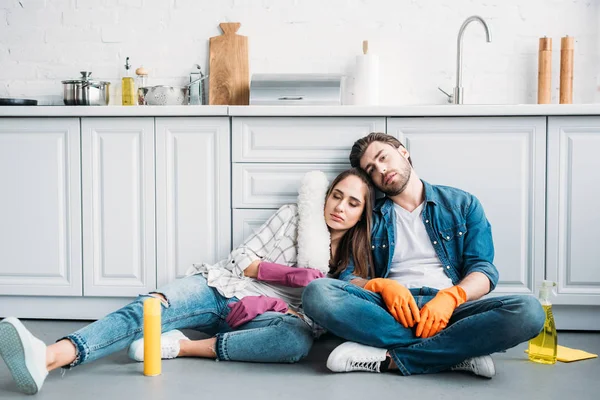 Coppia stanca seduta sul pavimento e appoggiata al bancone della cucina dopo la pulizia in cucina — Foto stock