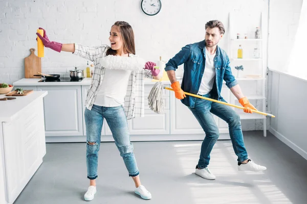 Girlfriend and boyfriend in rubber gloves having fun with mop in kitchen — Stock Photo
