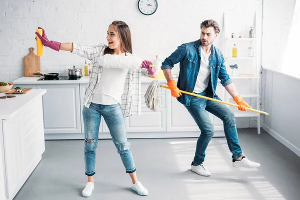 Novia y novio en guantes de goma divertirse con fregona en la cocina - foto de stock