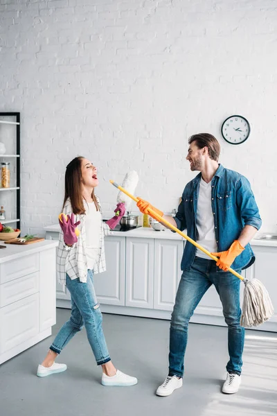 Casal em luvas de borracha se divertindo com esfregona e fingindo cantar na cozinha — Fotografia de Stock