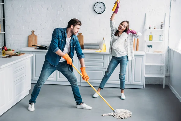 Casal em luvas de borracha se divertindo com esfregona durante a limpeza da cozinha — Fotografia de Stock