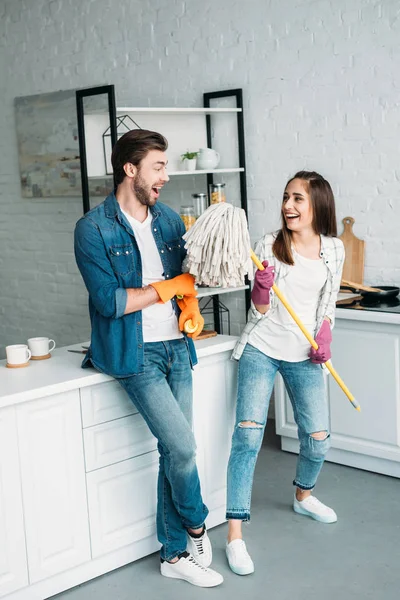 Pareja en guantes de goma divirtiéndose con fregona en la cocina y fingiendo cantar - foto de stock