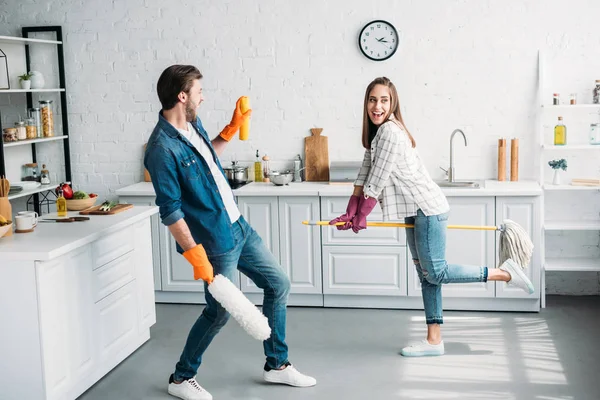 Casal em luvas de borracha se divertindo com esfregona na cozinha — Fotografia de Stock