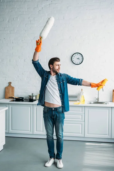 Mann posiert mit Staubbürste und Putzmittel in Küche — Stockfoto