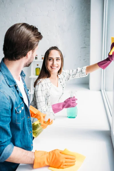 Casal sorrindo janelas de limpeza na cozinha juntos — Fotografia de Stock
