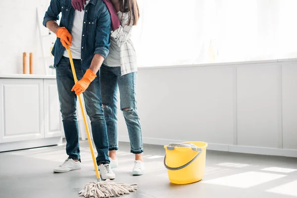 Cropped image of boyfriend cleaning floor in kitchen with mop and girlfriend hugging him — Stock Photo