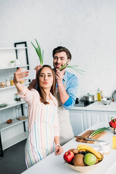 Пара приймає селфі, розважаючись під час приготування їжі на кухні — стокове фото