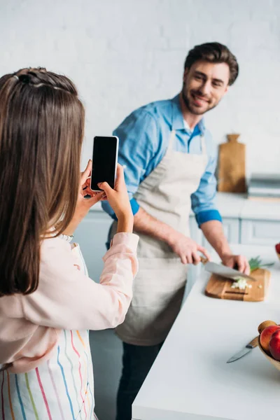 Girlfriend taking photo of boyfriend cutting vegetables in kitchen — Stock Photo