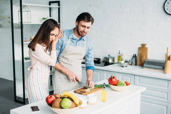 Novio cortando cebolla y llorando novia apoyándose en él en la cocina - foto de stock