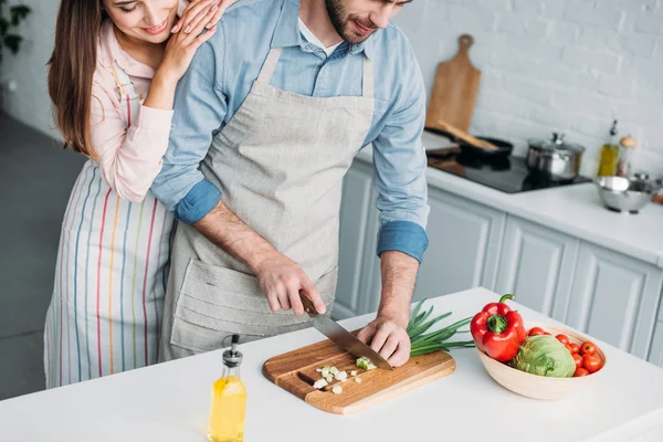 Обрізане зображення хлопця, який ріже овочі та дівчину, спираючись на нього на кухні — стокове фото
