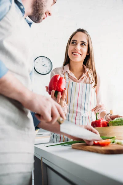 Freund schneidet Gemüse und Freundin gibt Paprika in Küche — Stockfoto