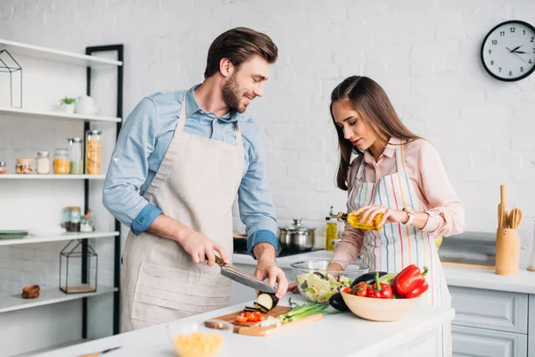 Novio cortar verduras y novia verter aceite en ensalada en la cocina - foto de stock