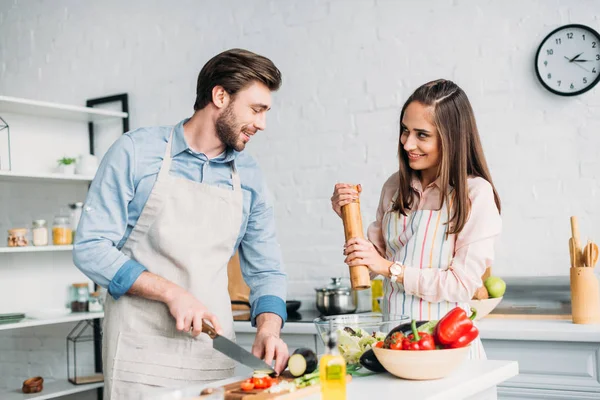 Novio cortar verduras y novia añadir especias a la ensalada en la cocina - foto de stock