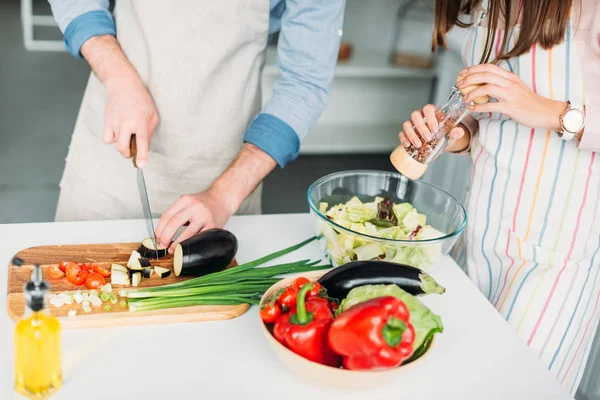 Immagine ritagliata del fidanzato che taglia verdure e fidanzata aggiungendo spezie all'insalata in cucina — Foto stock