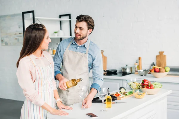 Boyfriend pouring wine into glass and looking at girlfriend in kitchen — Stock Photo