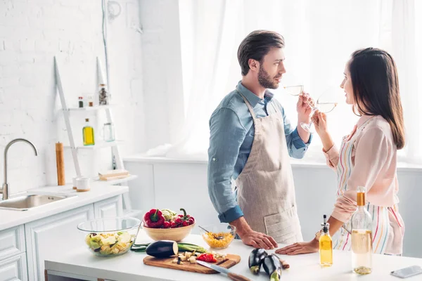 Pareja bebiendo vino y mirándose en la cocina - foto de stock