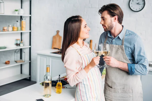 Couple cliquetis avec des verres à vin dans la cuisine et en se regardant — Photo de stock