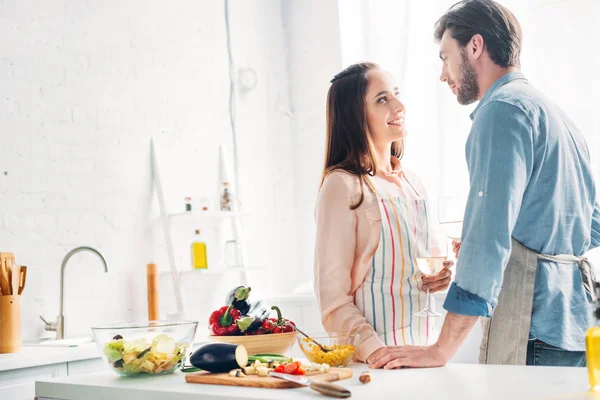 Pareja sosteniendo las gafas de vino y mirándose en la cocina - foto de stock