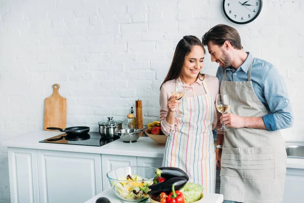 Smiling couple standing with glasses of wine in kitchen — Stock Photo