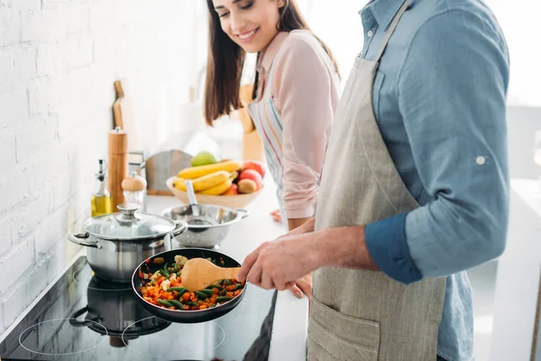 Imagem cortada de namorado fritando legumes no fogão elétrico na cozinha — Fotografia de Stock