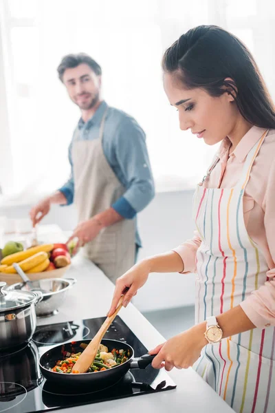 Girlfriend frying vegetables on frying pan in kitchen — Stock Photo