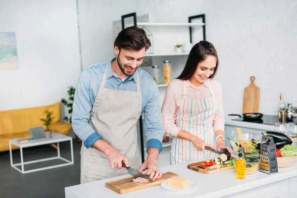 Couple cuisine et couper les légumes avec de la viande dans la cuisine — Photo de stock