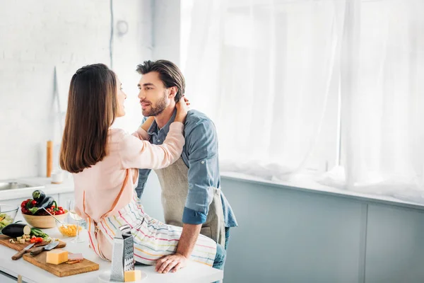 Couple hugging and girlfriend sitting on kitchen counter at home — Stock Photo