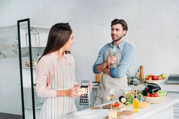 Novia rallar queso y guapo novio beber vino en la cocina - foto de stock