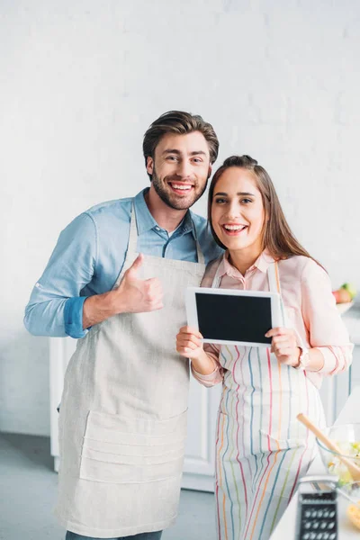Novio mostrando el pulgar hacia arriba y novia sosteniendo tableta en la cocina - foto de stock