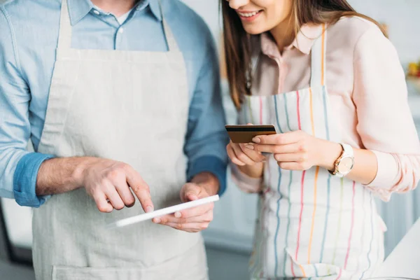 Обрезанное изображение пары покупок онлайн с планшетом и кредитной картой на кухне — стоковое фото