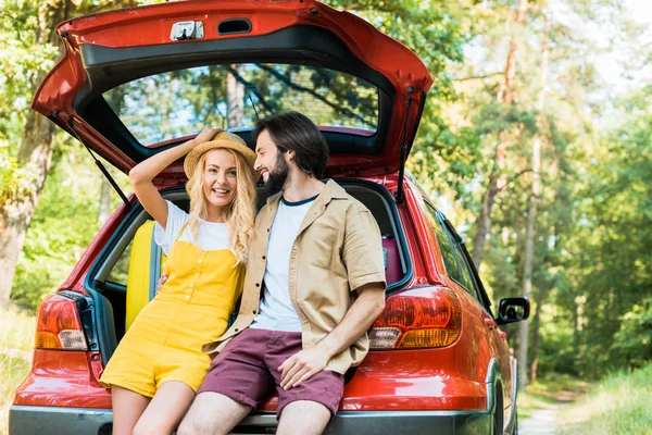 Couple souriant assis sur le coffre de la voiture dans la forêt — Photo de stock