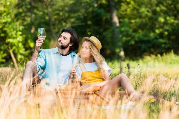 Pareja sentada en la hierba y beber vino en el picnic - foto de stock