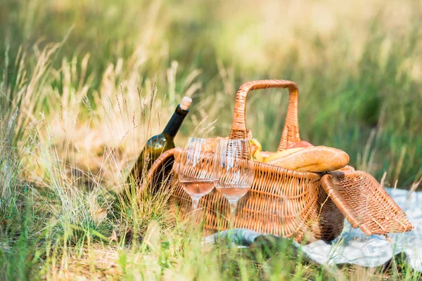 Wine bottle, basket with loaves on green grass at picnic — Stock Photo