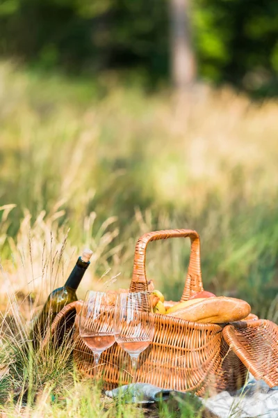Wine bottle, glasses and basket with loaves on grass at picnic — Stock Photo
