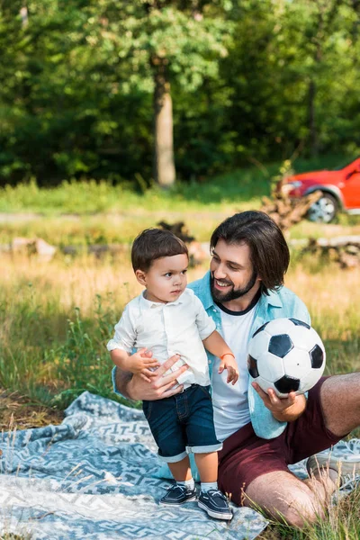 Feliz padre e hijo pequeño jugando con pelota de fútbol en el picnic - foto de stock