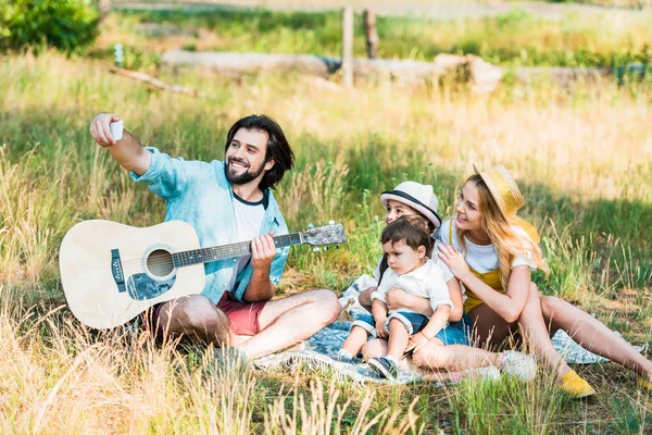 Father taking selfie of family with smartphone at picnic — Stock Photo