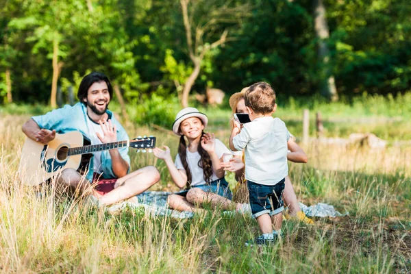 Маленький син фотографує сім'ю зі смартфоном на пікніку — стокове фото