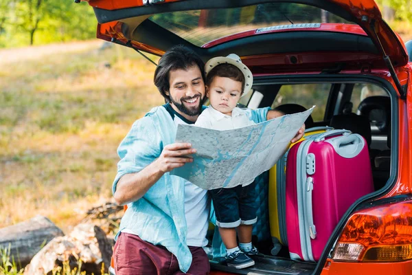 Souriant père et tout-petit fils regardant la carte au coffre de la voiture — Photo de stock