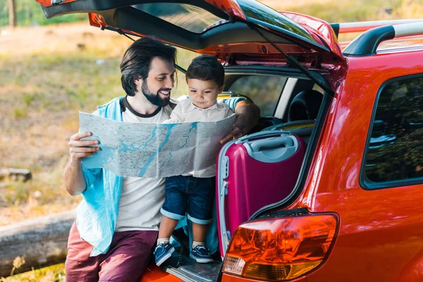Handsome father and adorable son looking at map at car trunk — Stock Photo