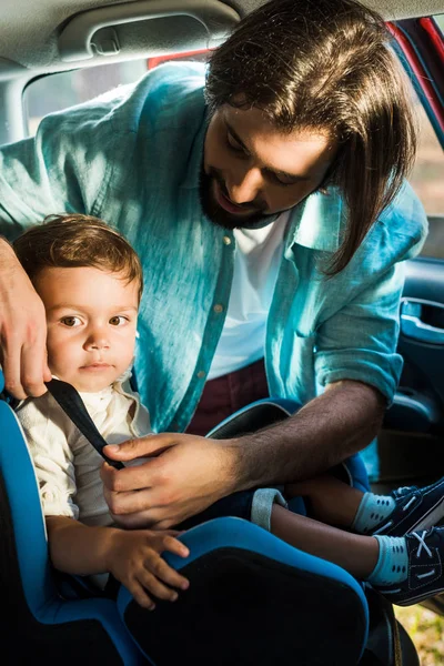 Батько кріплення чарівного сина на сидінні безпеки в машині — стокове фото