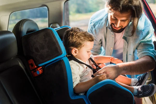 Handsome father fastening son in safety seat in car — Stock Photo