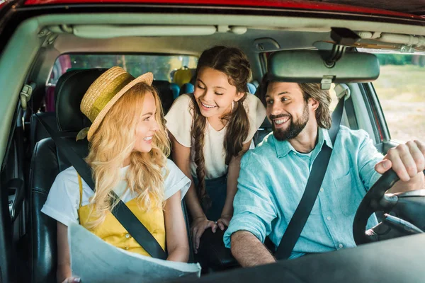 Sonrientes padres e hija viajando en coche con mapa - foto de stock