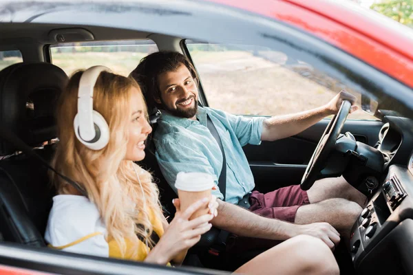 Couple voyageant en voiture, petite amie écoutant de la musique avec écouteurs et tenant du café à emporter — Photo de stock