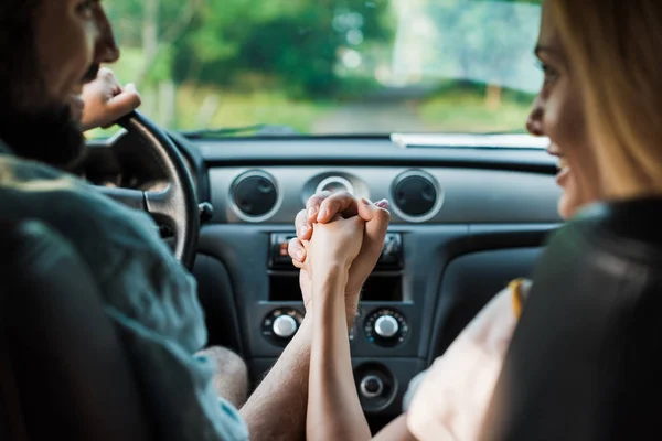 Smiling couple holding hands and sitting in car — Stock Photo