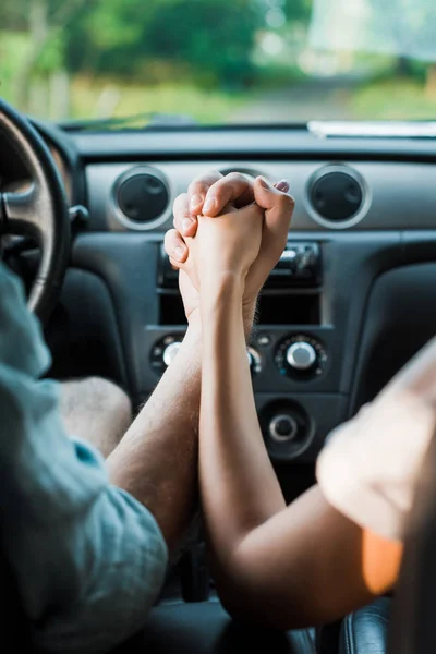 Cropped image of couple holding hands and sitting in car — Stock Photo