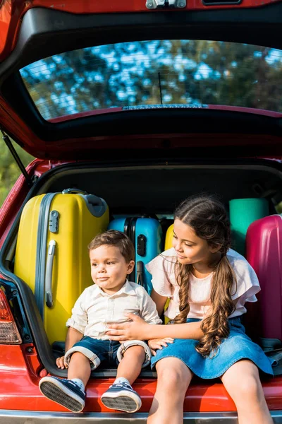 Fratello e sorella seduti vicino a borse da viaggio nel bagagliaio dell'auto — Foto stock