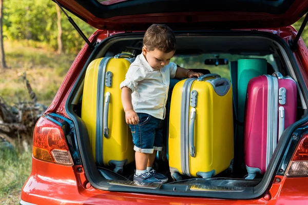 Adorable toddler boy standing with travel bags in car trunk — Stock Photo