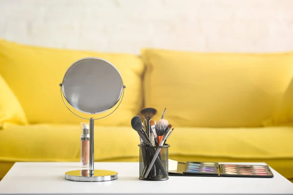 Крупним планом вид на жовтий диван, дзеркало, пензлі для макіяжу та косметику на кавовому столі — стокове фото